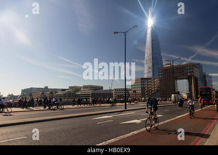 À vélo au travail à travers le pont de Londres au cours de la matinée, le trafic avec la lumière du soleil brillant sur le Shard building en arrière-plan. Banque D'Images