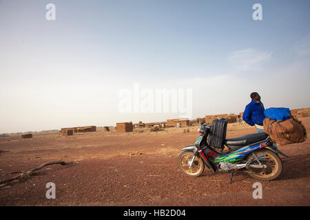 MOPTI, MALI - 1 janvier : Jeune homme migrants d'Afrique noire en attente devant son scooter chargé avec des bagages dans la campagne de Mopti Banque D'Images