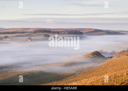 Mur d'Hadrien, à l'écart des TCA au lever du soleil d'une lumière dorée et la lumière brouillard dans la vallée de l'avant en décembre dans le Northumberland Banque D'Images