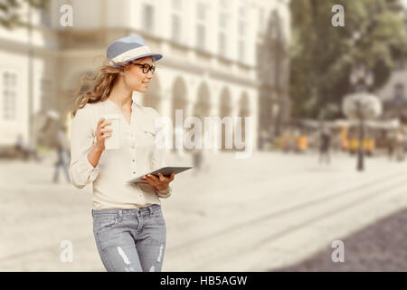 Belle jeune femme avec une tasse de café, boire du café, holding tablet dans ses mains, et traverser la rue contre urban city backgroun Banque D'Images