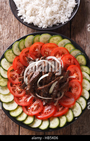 Rôti de bœuf mariné Lok Lak avec légumes frais et un plat de riz sur la table. Vue verticale d'en haut Banque D'Images