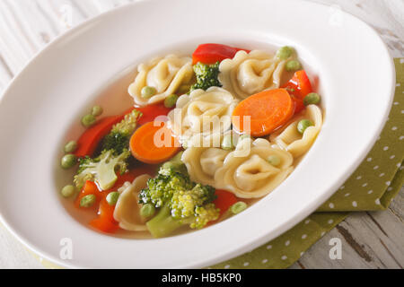 Sex tortellini soupe avec le brocoli, les pois, les carottes et le poivre gros plan sur la plaque sur la table. L'horizontale Banque D'Images