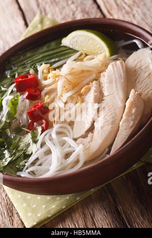 Soupe vietnamienne pho ga avec poulet et nouilles de riz, fèves germées et le chili dans un bol, close-up vertical. Banque D'Images