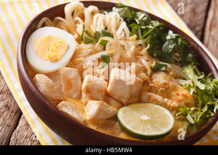 Laksa asiatique soupe épaisse avec du poulet, oeuf, pâtes de riz, de germes de soja et la coriandre dans un bol sur la table. L'horizontale Banque D'Images