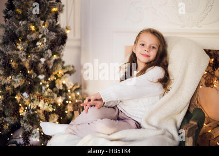 Little girl sitting on cosy enveloppé dans une couverture de l'arbre de Noël président matin à Accueil Banque D'Images