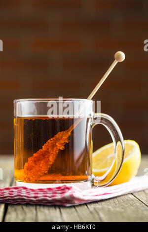 Tasse de thé avec du sucre cristal sur bâton en bois sur la vieille table en bois. Banque D'Images
