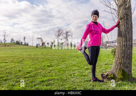 Jeune femme l'échauffement et l'étirement des jambes avant l'exécution par une froide journée d'hiver dans un parc. Banque D'Images