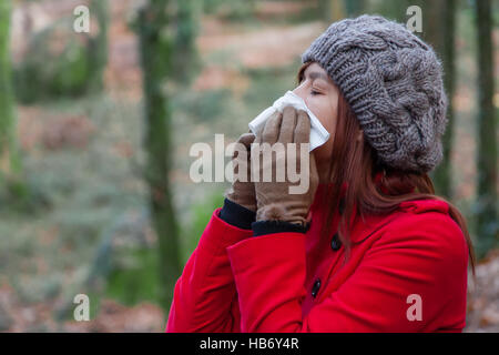 Jeune femme souffrant d'un rhume, la grippe ou les allergies s'être mouché le nez sur un mouchoir en papier blanc en hiver Banque D'Images