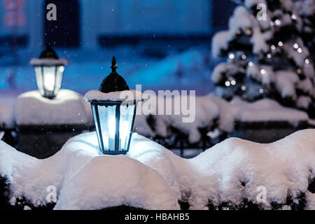 Les lampes allumées dans la rue enneigée nuit ville avec sapin et les lumières de Noël en arrière-plan Banque D'Images