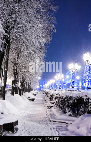 Nuit paysage d'hiver. ville rue d'arbres et de bancs de neige très éclairé avec réverbères. Banque D'Images