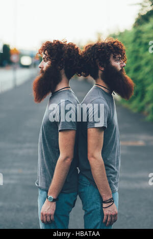 Portrait de jumeaux mâles adultes identiques aux cheveux rouges et barbes dos à dos sur le trottoir Banque D'Images