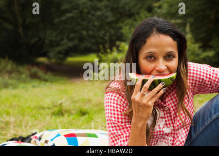 Portrait of young woman outdoors, sitting in field, eating watermelon Banque D'Images