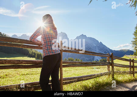 Mature Woman leaning against fence looking out at Dolomites de Sexten, ensoleillée, Tyrol du Sud, Italie Banque D'Images