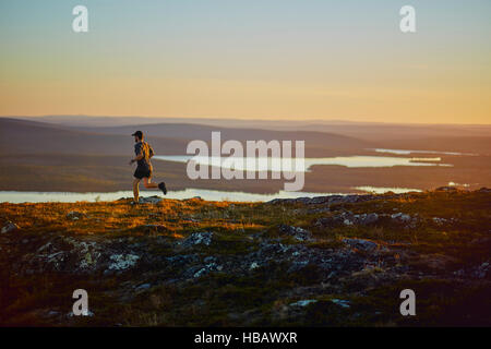Homme qui court sur la falaise au coucher du soleil, Keimiotunturi, Laponie, Finlande Banque D'Images