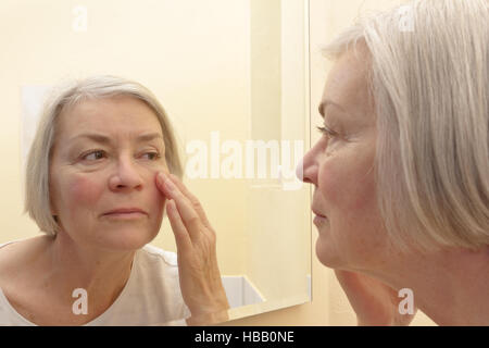 Concept de vieillissement, senior woman having a examiner de près les rides de son visage dans un miroir, de penser à la chirurgie esthétique Banque D'Images