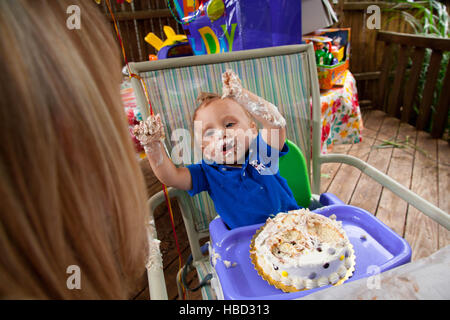 Young Caucasian boy fête son premier anniversaire, faire un gâchis avec gâteau à l'extérieur pendant l'été Banque D'Images