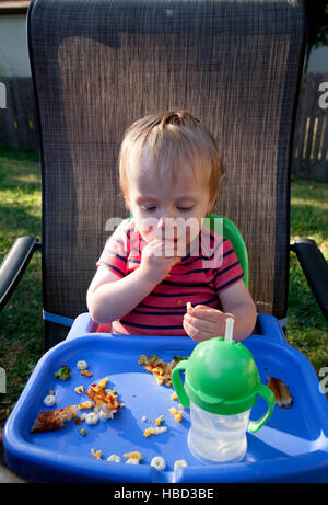 Caucasian baby garçon est assis dans une chaise haute et consomme des aliments à un pique-nique Banque D'Images