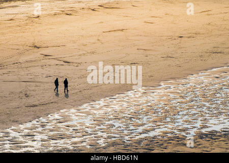 Deux personnes vu en silhouette et à distance sur la plage de Crantock à Newquay, Cornwall. Banque D'Images