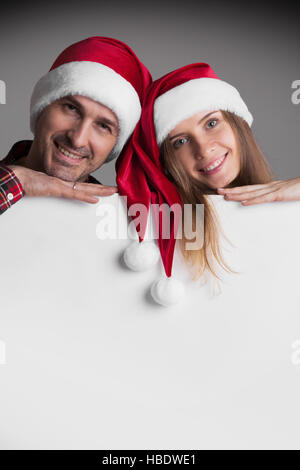 Happy smiling couple in Santa's hats avec white blank banner with copy space Banque D'Images