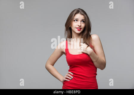 Belle femme réfléchie en chemise rouge à haut, sur fond gris Banque D'Images