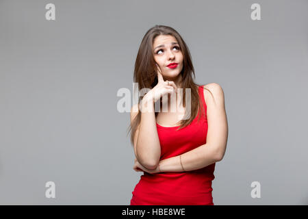 Belle femme réfléchie en chemise rouge à haut, sur fond gris Banque D'Images