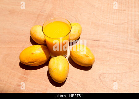 Jaune à maturité paraguayenne de mangues et de tasse de jus de mangue fraîche sur la table de bois, sous la lumière du soleil lumineuse Banque D'Images