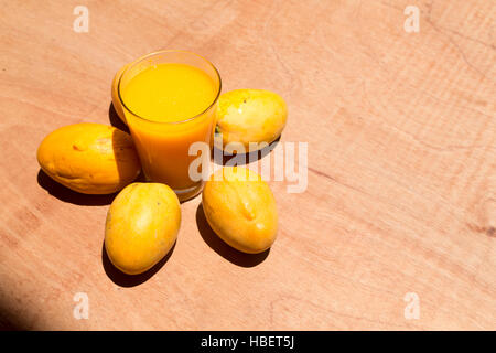 Jaune à maturité paraguayenne de mangues et de tasse de jus de mangue fraîche sur la table de bois, sous la lumière du soleil lumineuse Banque D'Images