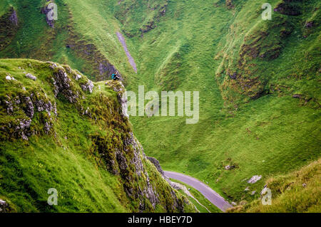 Femme sur un promontoire rocheux avec road ci-dessous, Peak District, Derbyshire, Royaume-Uni. Banque D'Images