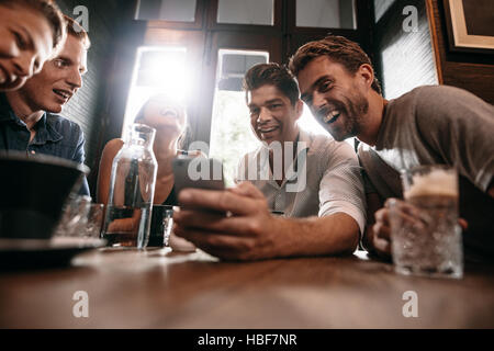 Groupe d'amis assis ensemble dans un café à la recherche de téléphone intelligent et souriant. Jeune homme montrant quelque chose à ses amis sur son téléphone cellulaire. Banque D'Images