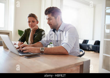 Shot of young man working on laptop with woman sitting by. Couple assis ensemble à table et à l'aide d'ordinateur portable. Banque D'Images