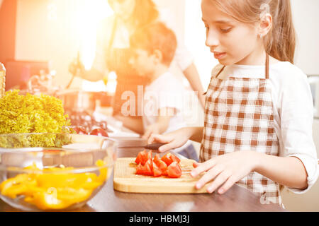 Jeune adolescente, avec sa famille de cuisson dans la cuisine. Cute girl hacher les tomates pour la salade Banque D'Images