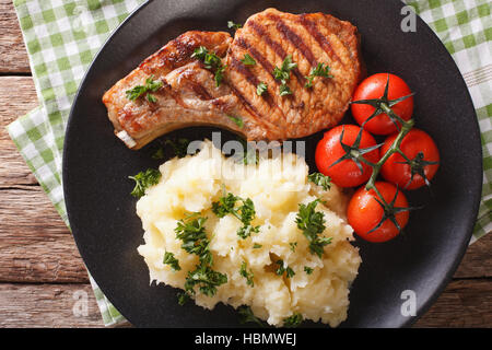 Porc grillé T-bone steak garni avec de la purée de pommes de terre et de tomate sur une assiette. Vue du dessus horizontale Banque D'Images