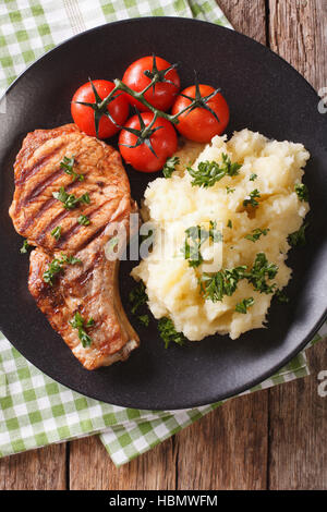 Porc grillé T-bone steak garni avec de la purée de pommes de terre et de tomate sur une assiette. vertical Vue de dessus Banque D'Images