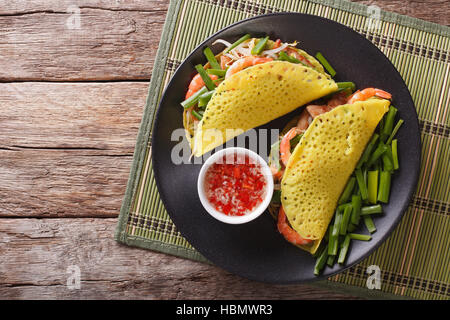 Le vietnamien Banh Xeo crèpes farcies avec le porc, les crevettes, les oignons et les fèves germées et une sauce épicée libre sur une plaque sur la table. Vue horizontale à partir de Banque D'Images