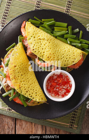 Le vietnamien Banh Xeo crèpes farcies avec le porc, les crevettes et les fèves germées et une sauce sauce nuoc cham libre sur une assiette. vertical Vue de dessus Banque D'Images