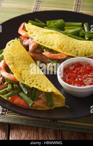 Le vietnamien Banh Xeo crèpes farcies avec le porc, les crevettes, les oignons et les fèves germées et une sauce épicée libre sur une plaque verticale sur la table. Banque D'Images