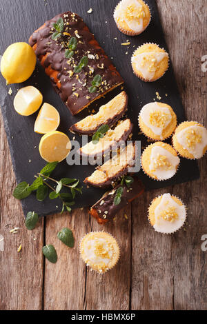 Tranches de citron gâteau au chocolat et citron muffins avec du glaçage et le zeste de close-up sur la table. vertical Vue de dessus Banque D'Images