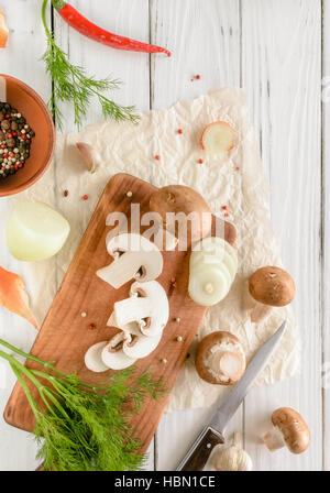 Brown champignon champignons sur une planche à découper. Bureau en bois blanc, les herbes et les oignons. Banque D'Images