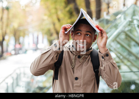 Photo de jeunes heureux homme africain avec un ordinateur portable sur sa tête à l'extérieur. Regarder de côté. Banque D'Images