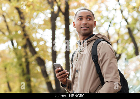 Photo de cheerful young African man holding son téléphone dans les mains et à côté. Banque D'Images