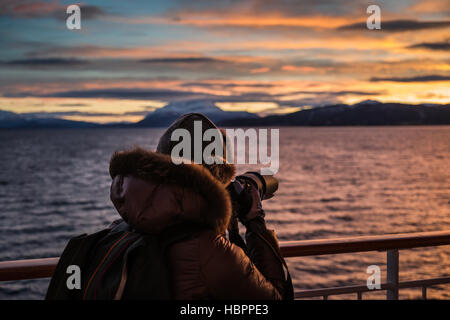 Une femelle adulte saisit une image alors que sur l'Hurtigruten au coucher du soleil, la Norvège. Banque D'Images