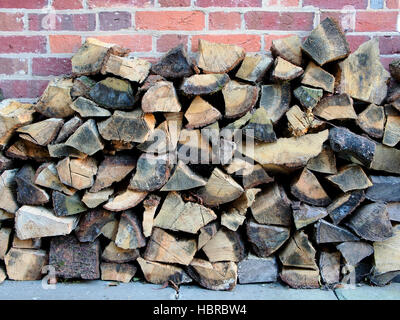 Une pile de bûches stockés sous abri contre un mur de brique rouge prêt à être gravé sur un feu ouvert ou un poêle. Banque D'Images