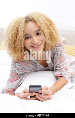 Détendez-vous dans le lit. La femme dans la chambre. Jeune femme écrit un message sur le téléphone en position couchée dans le lit Banque D'Images