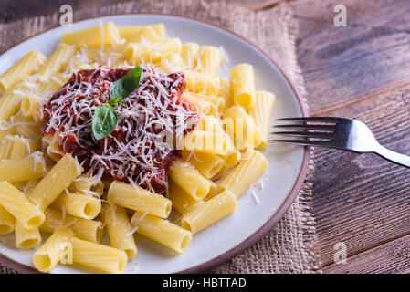 Les pâtes à la sauce tomate et le parmesan sur la table en bois naturel avec une fourchette. Banque D'Images