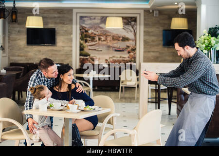 La famille, la parentalité, la technologie, les gens heureux concept - mère, père et petite fille qui a demandé à prendre une photo par serveur smartphone Blackberry Banque D'Images