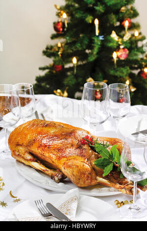 Oie rôtie sur une table décorée de fête, derrière un arbre de Noël décoré Banque D'Images