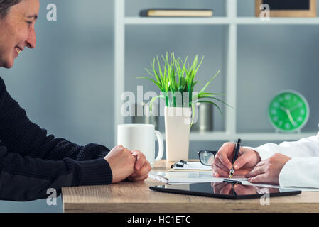 Satisfaits happy female patient in hospital Office après examen médical alors que l'écriture est docteur en médecine et recommandations - aucune prescription requise Banque D'Images