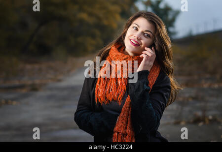 Portrait d'une jeune belle fille en rouge écharpe en tricot est un plaisir de parler au téléphone. La marche à l'extérieur dans la soirée Banque D'Images