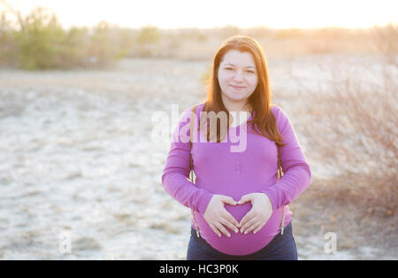 Belle Jeune femme enceinte sur un fond de coucher du soleil. 9e mois de grossesse. Banque D'Images