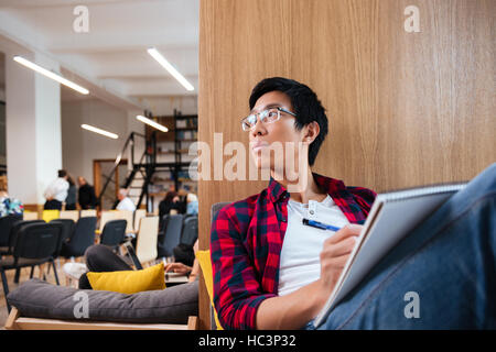 L'Asie concentre student studying in university library assis sur un canapé. À côté. Banque D'Images